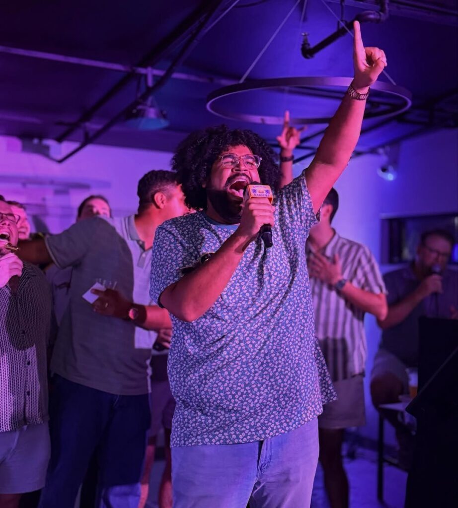 Man singing into a microphone at a karaoke party with purple ambient lighting.