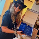 Woman in a 40th birthday hat holding a blue skincare gift set box.