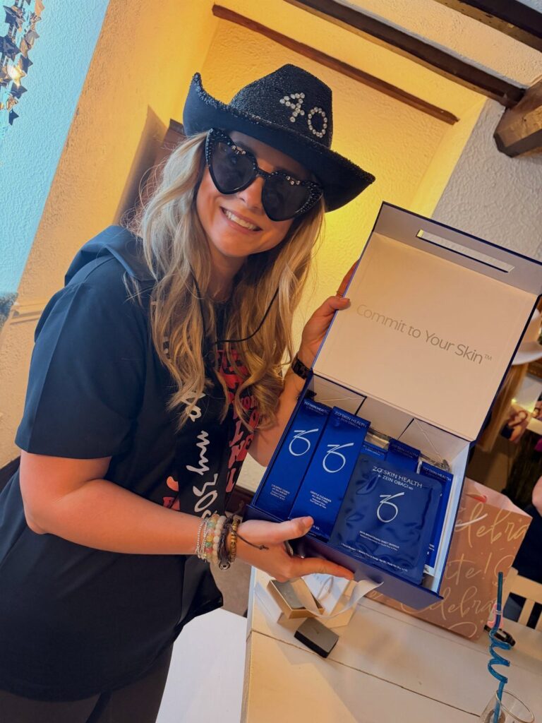Woman in a 40th birthday hat holding a blue skincare gift set box.