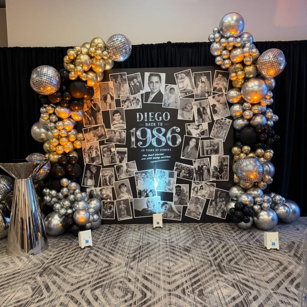 Birthday backdrop with black and white photos, gold and silver balloons, and disco balls.