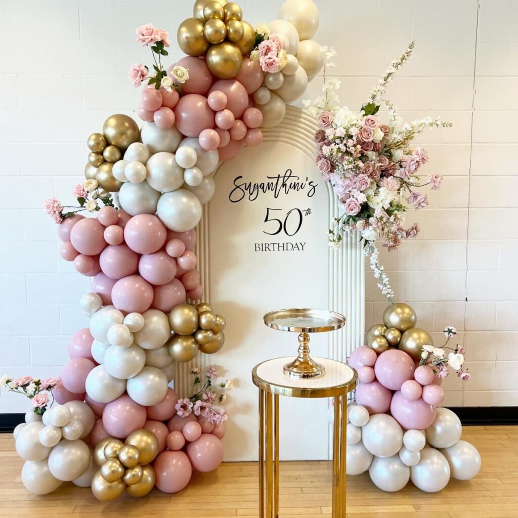 Pink, white, and gold balloon arch with floral accents for a 50th birthday.