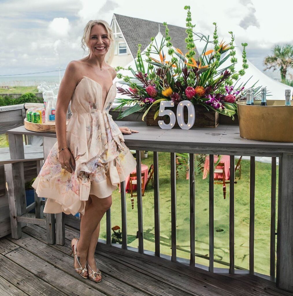 Woman in floral dress posing next to light-up 50 sign on a deck