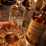 Engraved crystal whiskey glass and decanter set next to a scotch bottle.