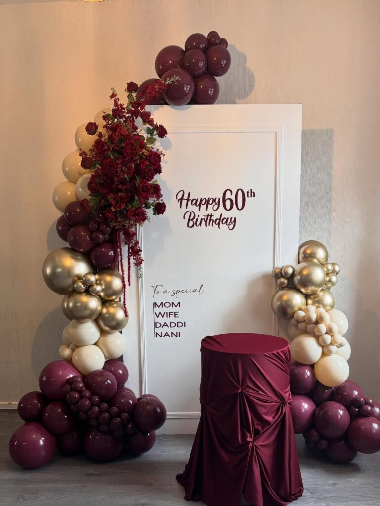 Birthday backdrop with burgundy and gold balloons, red flowers, and 60th birthday text.