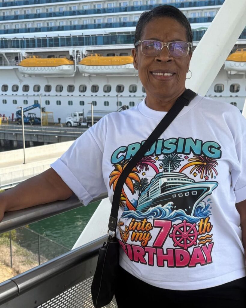 Older woman in 70th birthday cruise shirt standing before a large cruise ship