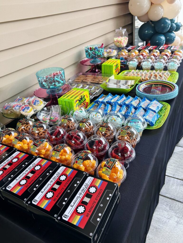 Party dessert table featuring colorful sweets and cassette tape themed treat boxes.