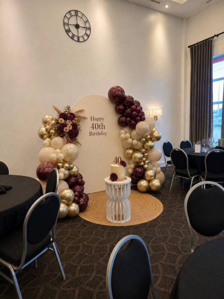 Burgundy, gold, and cream balloon arch surrounding a 40th birthday backdrop and cake.