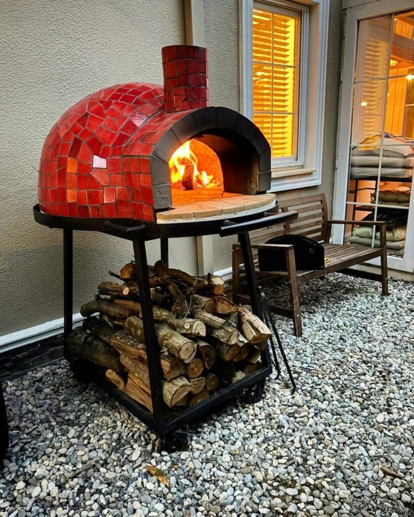 Red tiled outdoor pizza oven with fire inside on a black metal stand