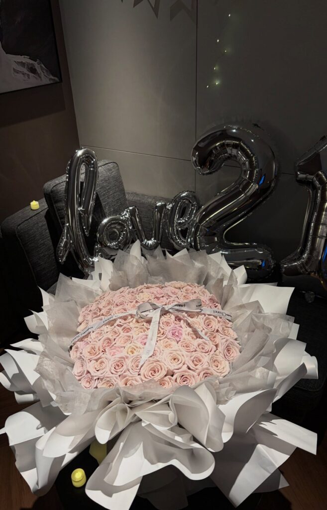 Heart-shaped pink rose bouquet with silver love 21 balloons in the background