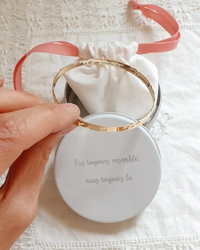 Gold engraved bangle bracelet held over a white gift tin and pouch.