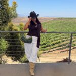 Woman holding a glass of wine overlooking a lush green vineyard landscape.