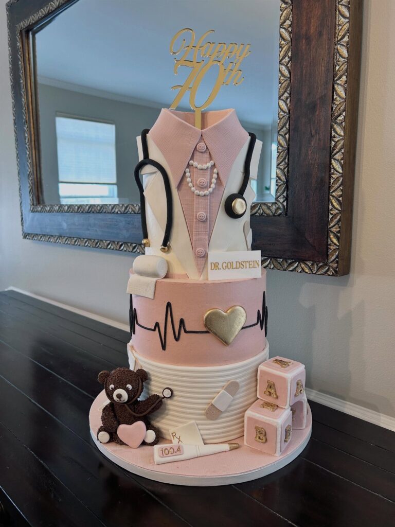 Three-tier doctor-themed birthday cake with a gold Happy 70th topper and medical details.