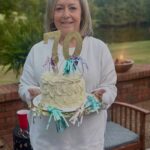 Woman holding a white birthday cake with a gold 70 topper outdoors