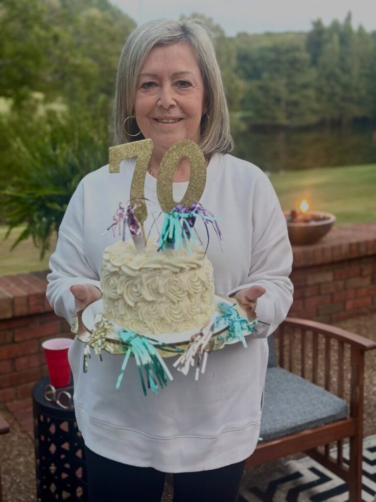 Woman holding a white birthday cake with a gold 70 topper outdoors