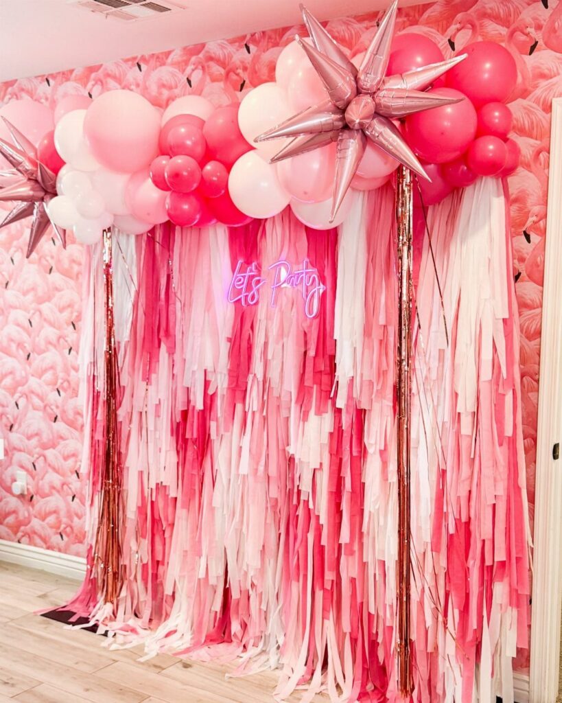 Pink and white balloon arch with tinsel backdrop and neon sign.