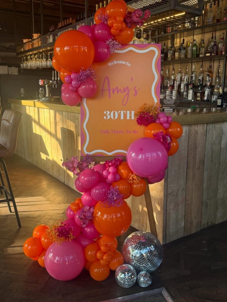 Birthday decoration with pink and orange balloons and a 30th birthday sign in a bar