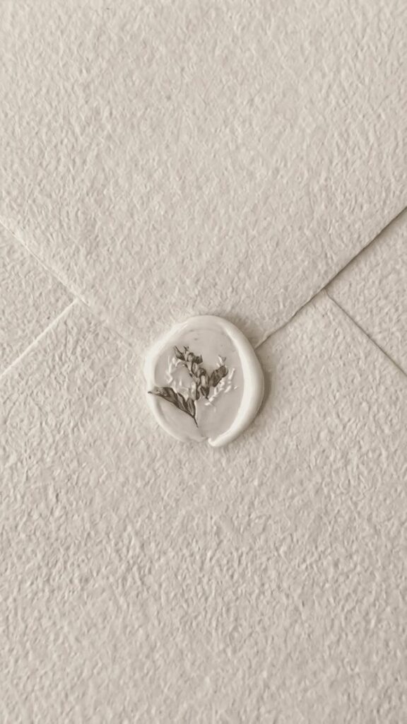 Cream textured envelope sealed with a white wax seal and dried flower sprig.