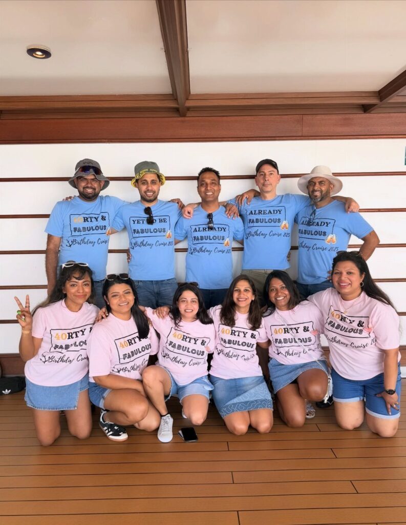 Group of adults in matching birthday t-shirts posing on a cruise ship deck.