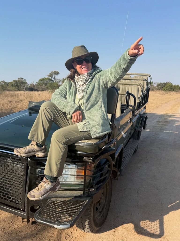 Woman in safari gear sitting on a vehicle in the African savanna pointing away