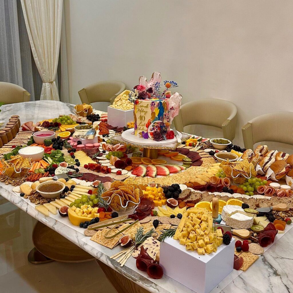 Lavish charcuterie and cheese spread on a marble table with a colorful birthday cake.
