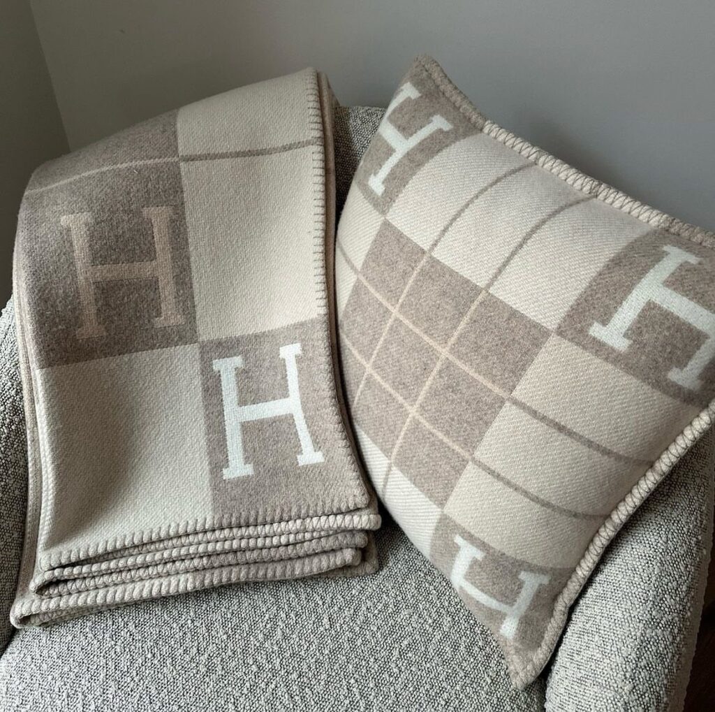 Beige and tan checkered Hermès blanket and matching pillow on a grey chair.